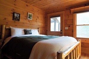 A wooden cabin room with a bed, a window, and two framed pictures on the wall.