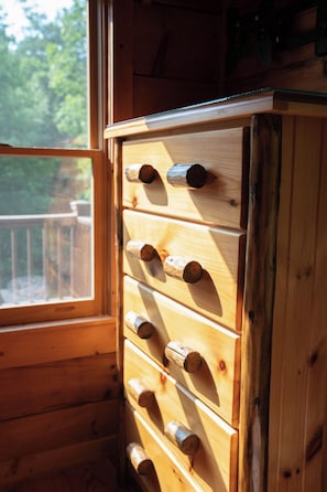 A wooden cabinet with multiple drawers, a window with a view of greenery, and a wooden railing outside.