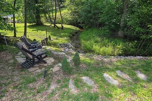 A natural outdoor area with a stone pathway, a bench, and a small stream.