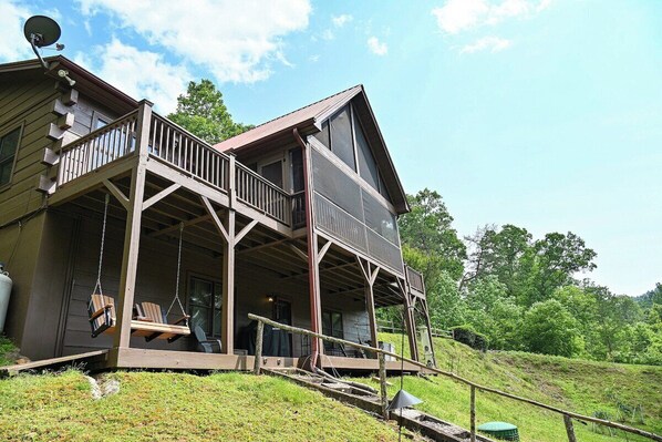 A two-story wooden house with a porch and swing chairs.