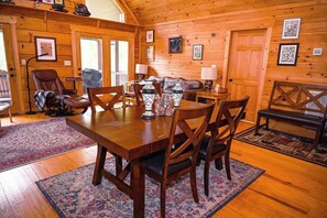 A wooden interior with a dining table, chairs, a sofa, and a fireplace.
