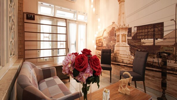 A room with a sofa, chairs, a table with a vase of flowers, and a mural of a building.