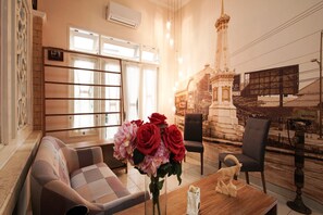 A room with a sofa, chairs, a table with a vase of flowers, and a mural of a building. - Collection O 3986 Just 11 Boutique Residence Syariah (Ngaglik)