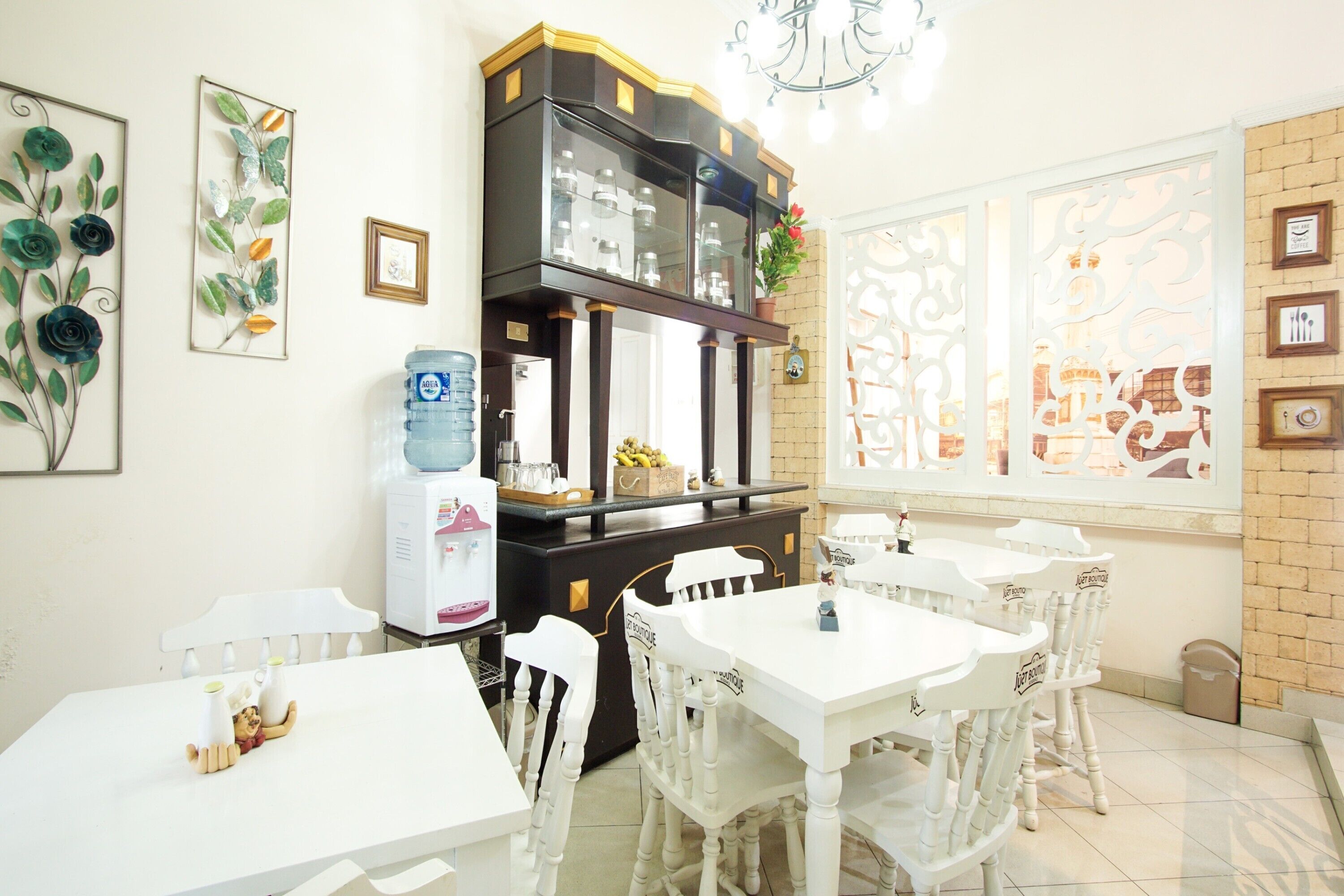 Un comedor con mesas y sillas blancas, un dispensador de agua y decoración en la pared.