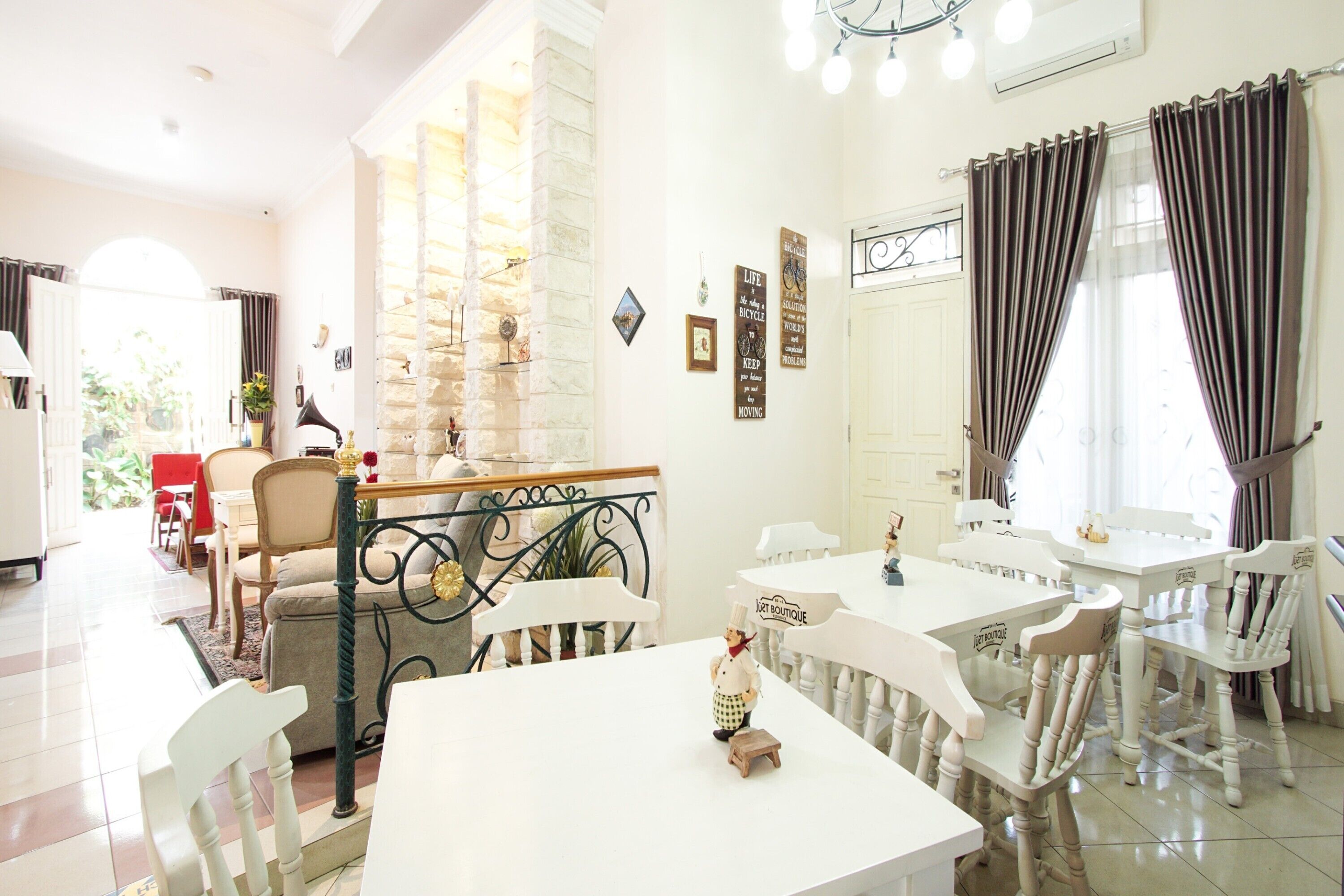 A dining area with white tables and chairs, a small figurine on a table, and a staircase with a stone wall.