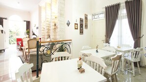 A dining area with white tables and chairs, a small figurine on a table, and a staircase with a stone wall.