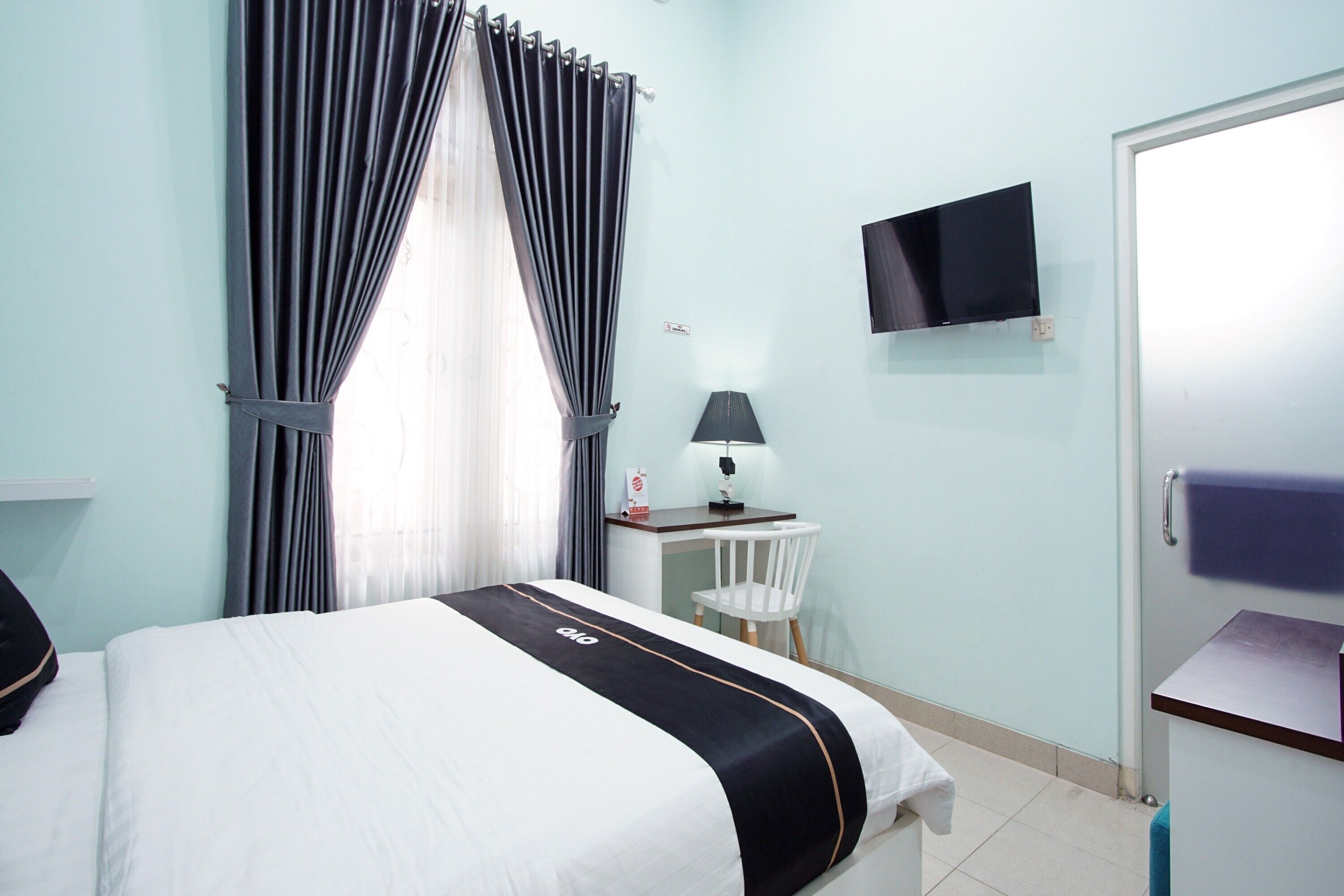 A hotel room with a bed, a desk, a chair, a TV, and a door.