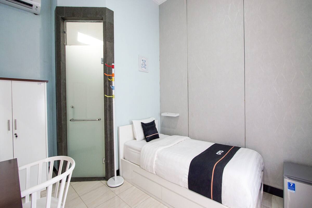Een slaapkamer met een enkel bed, een witte stoel, een kledingkast en een klein bureau.