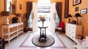 A hotel lobby with a round table, a potted plant, a red chair, and a white cabinet.