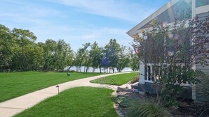 A landscaped area with a pathway, trees, and a building with large windows. - River Shores Cottage (Ottawa)