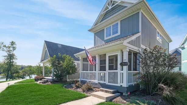 A two-story house with a porch, a flag, and a number sign. - River Shores Cottage (Ottawa)