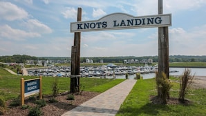 A marina with boats, a wooden sign reading 'KNOTS LANDING,' and a pathway leading to a grassy area. - River Shores Cottage (Ottawa)
