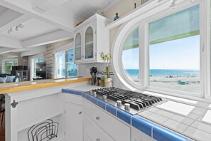 A modern kitchen with a large window offering a beach view, white cabinetry, and a blue-tiled backsplash. - Rio Del Mar Boathouse - steps from the beach (Aptos)
