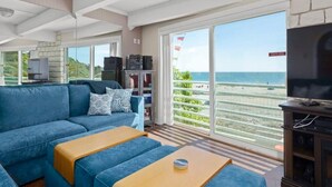 A living room with a large sofa, a coffee table, a television, and a view of the beach. - Rio Del Mar Boathouse - steps from the beach (Aptos)