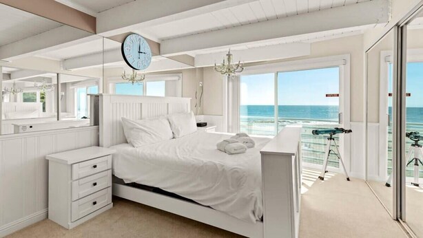 A bedroom with a bed, a dresser, a large window with a view of the ocean, a chandelier, and a telescope. - Rio Del Mar Boathouse - steps from the beach (Aptos)