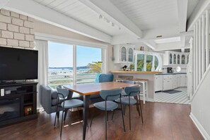 A modern kitchen with white cabinets, a wooden dining table, and a large window overlooking a beach. - Rio Del Mar Boathouse - steps from the beach (Aptos)
