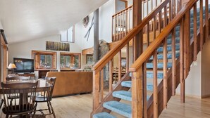 Un salón espacioso con una escalera de madera, una mesa de comedor con sillas y una televisión.