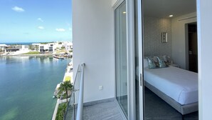 A balcony with a view of a marina and buildings, a bed with pillows, and a sliding glass door. - Nuevo Departamento con Playa Privada en Puerto Cancún (Cancún)