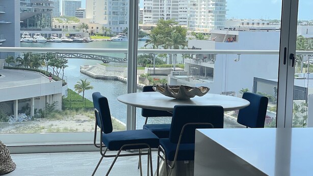 A modern room with a large window overlooking a marina and high-rise buildings. - Nuevo Departamento con Playa Privada en Puerto Cancún (Cancún)