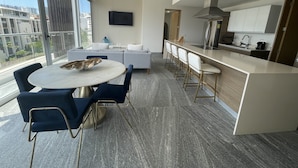 A modern kitchen with a central island, bar stools, and a dining area with a round table and chairs. - Nuevo Departamento con Playa Privada en Puerto Cancún (Cancún)