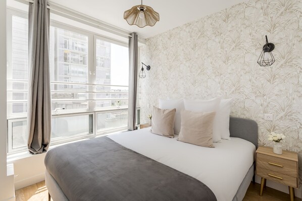 Une chambre moderne avec un grand lit, une vue sur la ville par la fenêtre et une applique murale décorative.