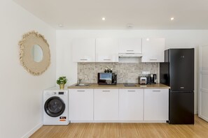 A compact kitchen with white cabinets, a black refrigerator, a washing machine, and a microwave. - Family Suite - Tour Eiffel - Finlay (Paris)