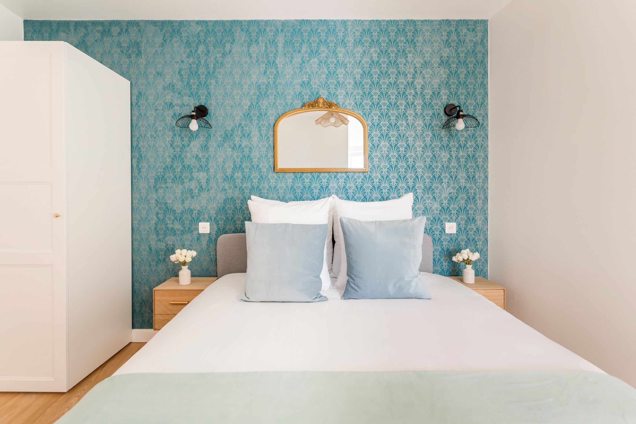 A bedroom with a bed, two bedside tables, a mirror, and wall sconces.