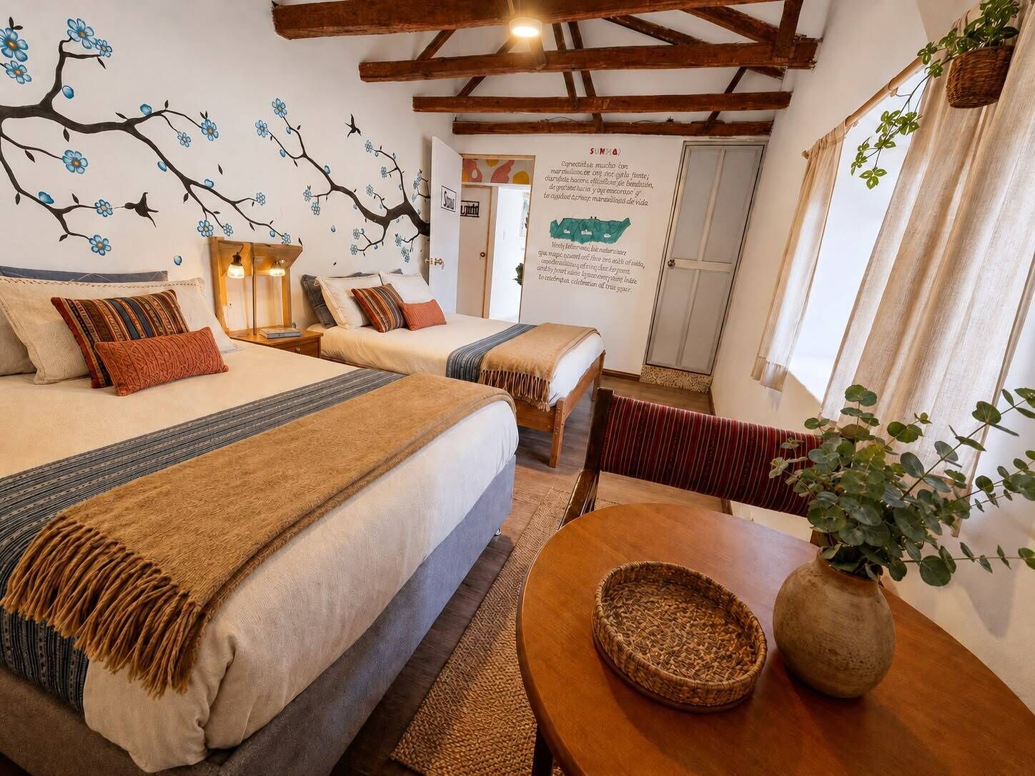 Ein Hotelzimmer mit zwei Betten, einem Holztisch, einem gewebten Korb und einer Blumentopf-Pflanze.