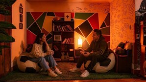 Two people sitting on bean bags in a room with a colorful geometric wall design, a bookshelf, and a lit candle. - valle verde (Urubamba)