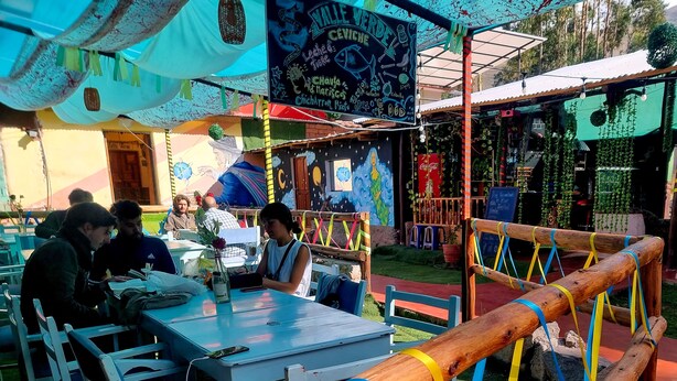 An outdoor dining area with tables and chairs, a wooden fence, and a mural on the wall. - valle verde (Urubamba)