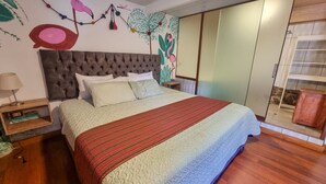 A bedroom with a tufted headboard, a bed with a patterned bedspread, a nightstand with a lamp, and a wall with a mural. - valle verde (Urubamba)