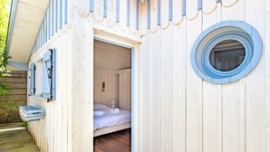 A small, wooden cabin-style room with a single bed, a window, and a door leading outside.