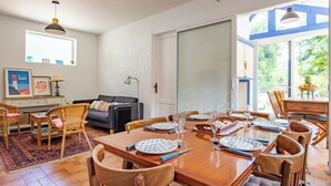 A dining area with a wooden table set for six, surrounded by wooden chairs. A black radiator is visible on the wall, and a sofa is placed against the wall.