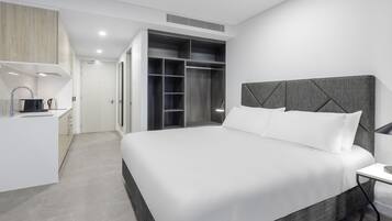 Ein modernes Hotelzimmer mit einem großen Bett, einem eingebauten Kleiderschrank, einer kleinen Küchenzeile und einem Nachttisch.