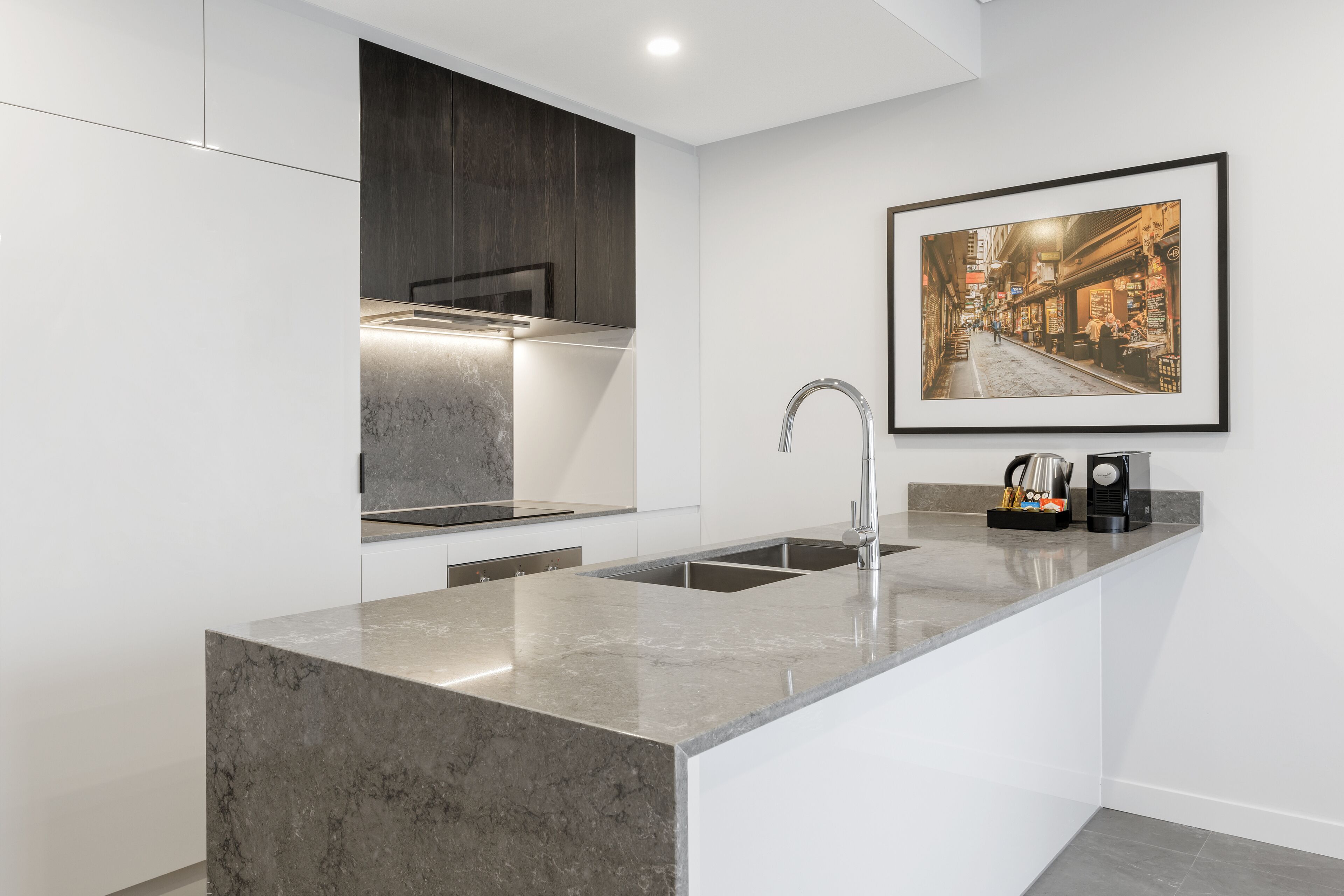 A modern kitchen with a marble island, stainless steel sink, and a framed cityscape photo on the wall.