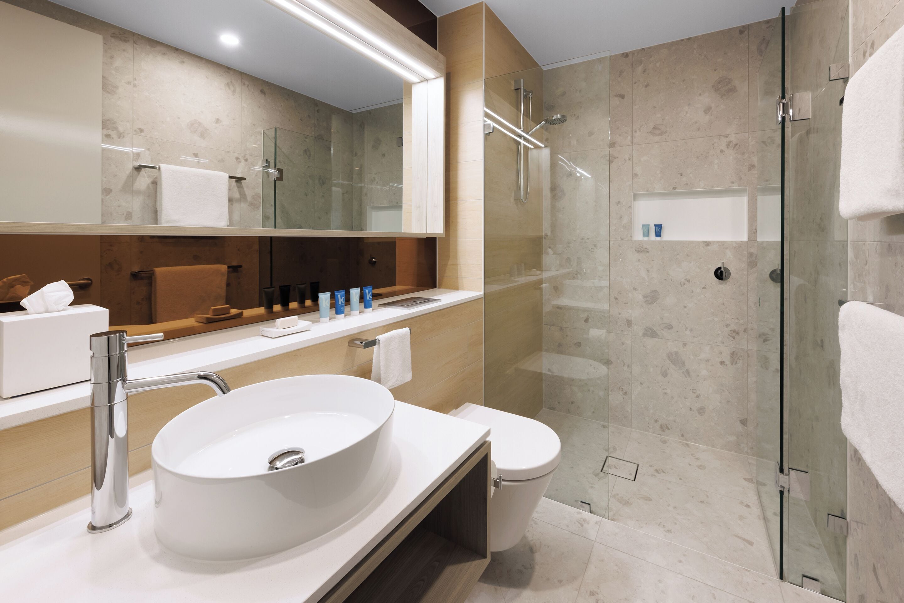 A modern bathroom with a large white sink, a glass-enclosed shower, and a mirror above the sink.