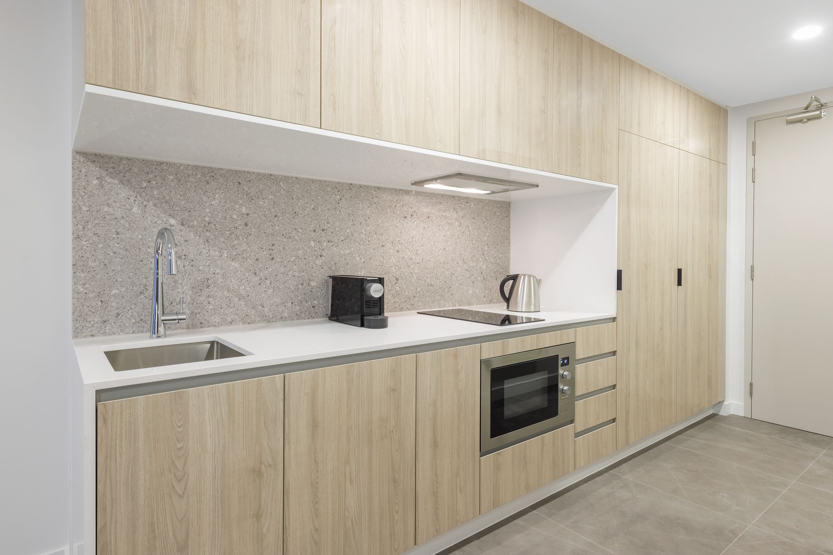 A modern kitchen with wooden cabinets, a stainless steel sink, a coffee maker, and an oven.