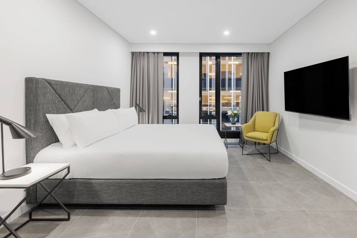 A modern hotel room with a large bed, a desk, a chair, and a TV.