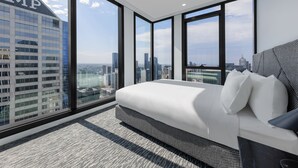 A modern hotel room with a large bed, a view of the cityscape, and a large window.