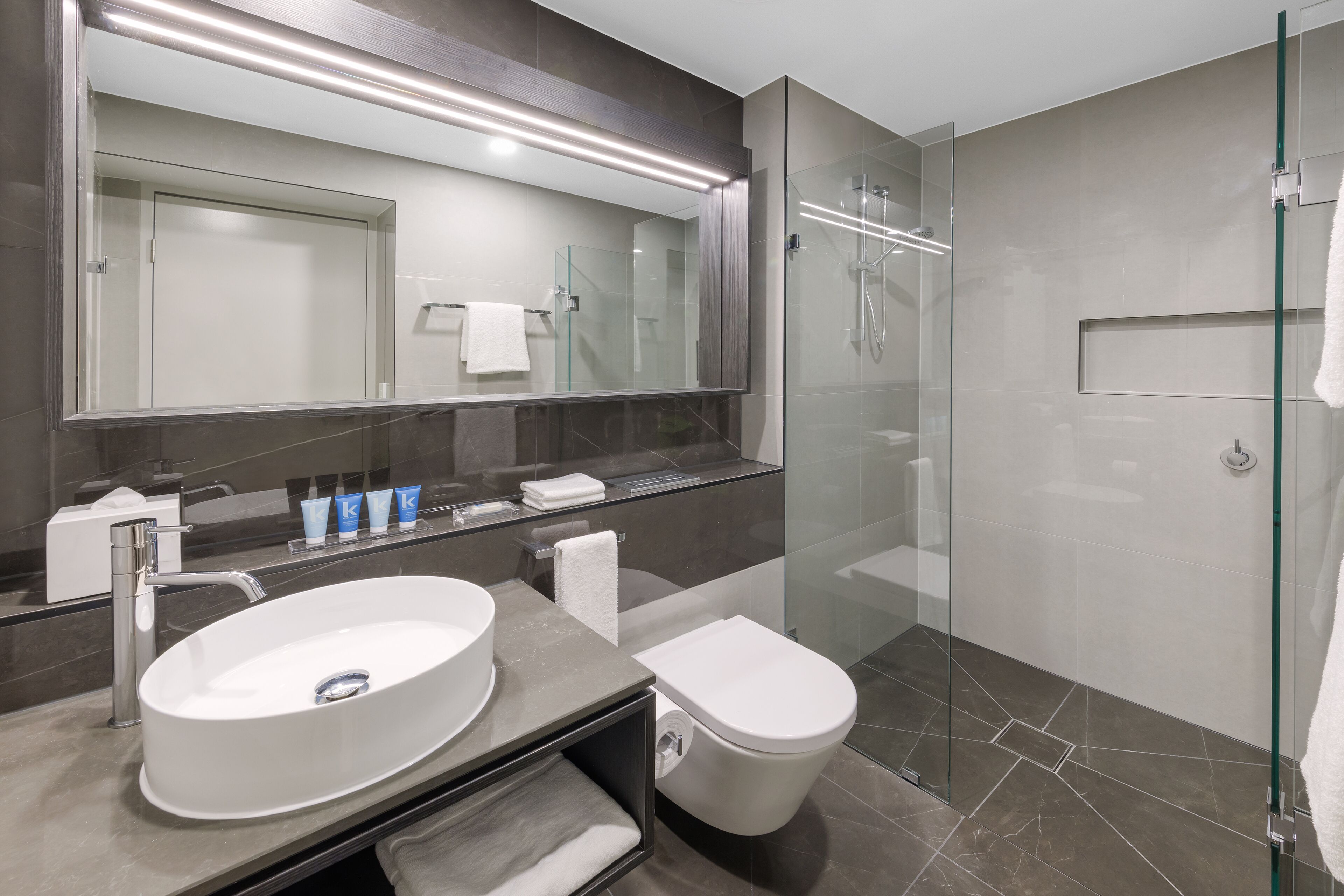A modern bathroom with a large mirror, a round sink, a toilet, and a glass-enclosed shower.