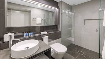 A modern bathroom with a large mirror, a round sink, a toilet, and a glass-enclosed shower.