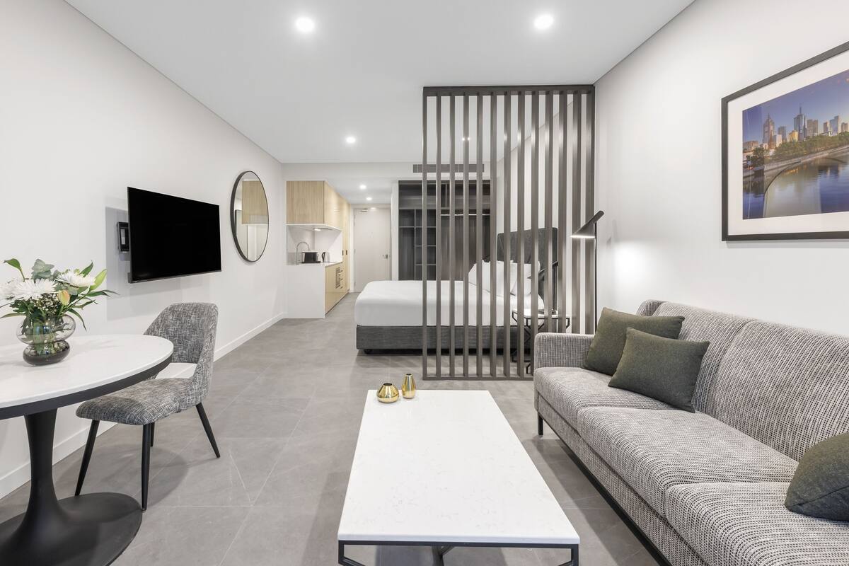 A modern living room with a sofa, a coffee table, a TV, and a dining area with chairs.