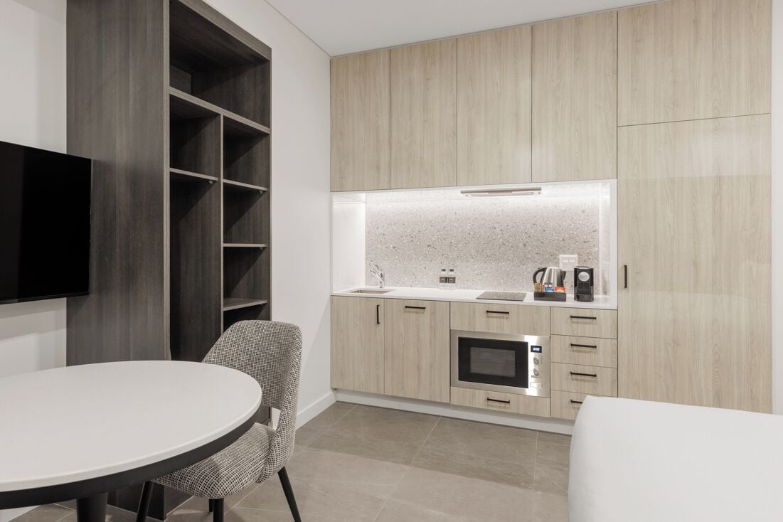 Une cuisine moderne dotée d’appareils électroménagers intégrés, un coin repas avec une table ronde et un téléviseur fixé au mur.