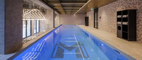 Una piscina interior moderna con un diseño geométrico de azulejos, un candelabro y una pared revestida con un patrón geométrico.
