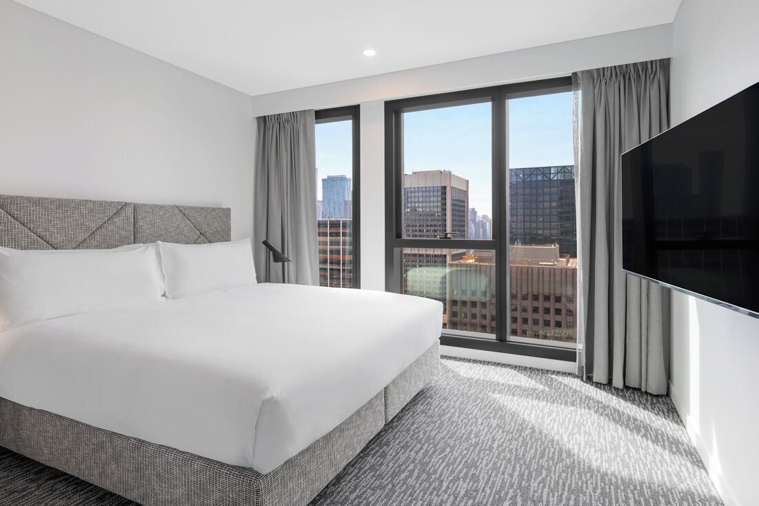 A hotel room with a large bed, a flat-screen TV, and a city view.
