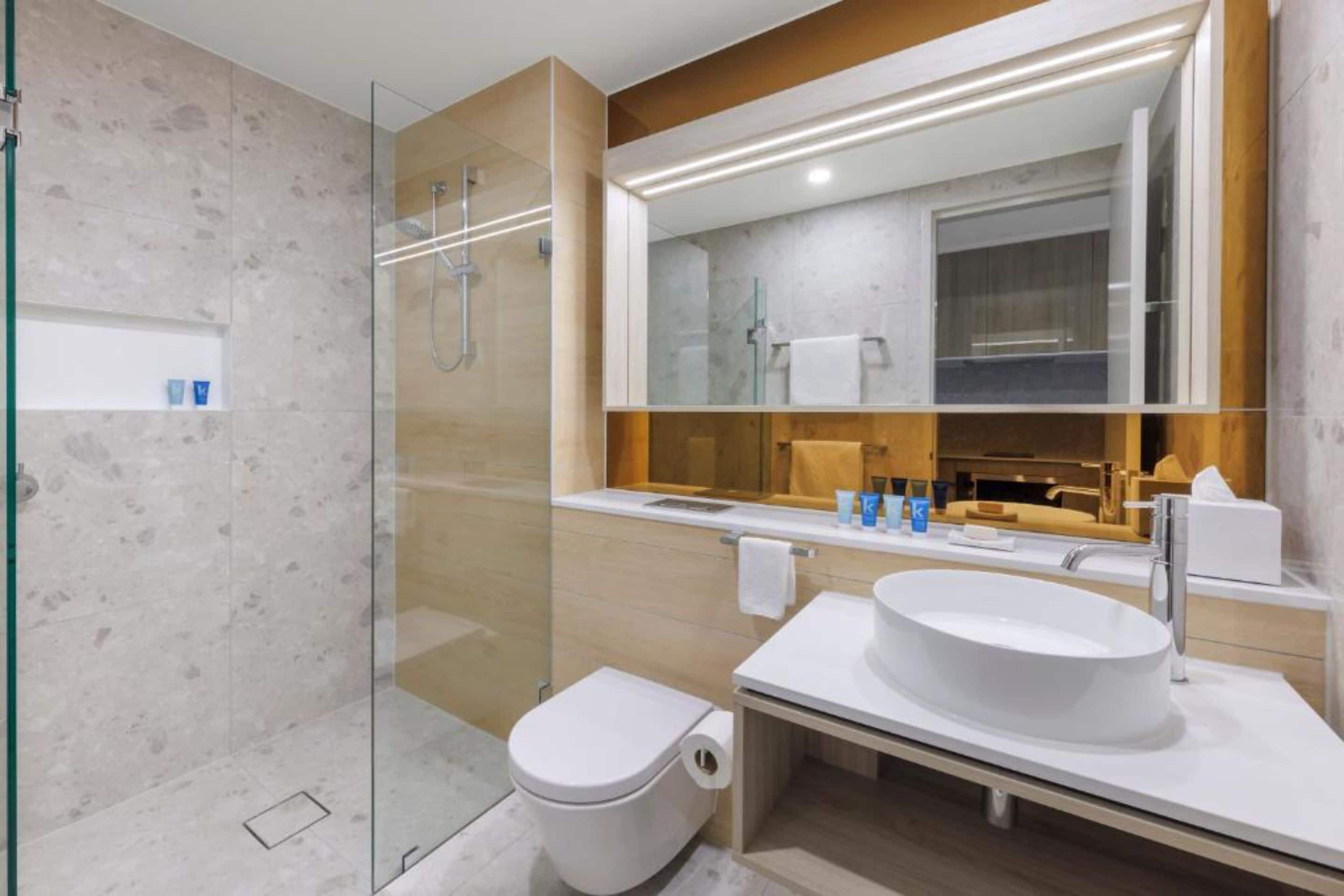 A modern bathroom with a glass-enclosed shower, a white sink, and a large mirror.