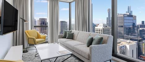 A modern living room with a large window, a sofa, a yellow armchair, and a flat-screen TV.