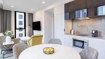 Una habitación de hotel moderna con comedor, una cocina equipada con microondas y un televisor de pantalla plana.
