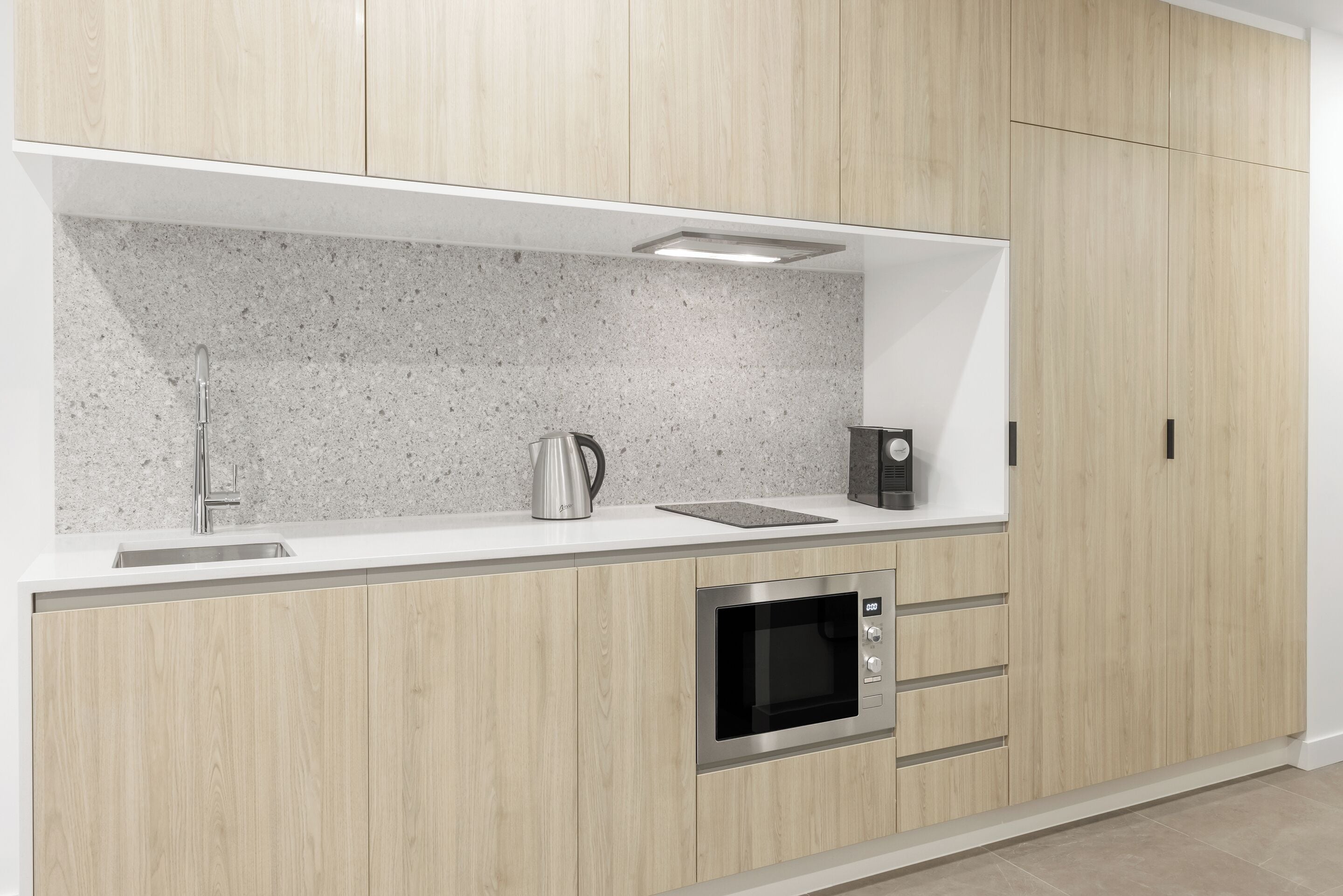 Une cuisine moderne avec des meubles en bois, un évier en acier inoxydable, une bouilloire et un four encastré.