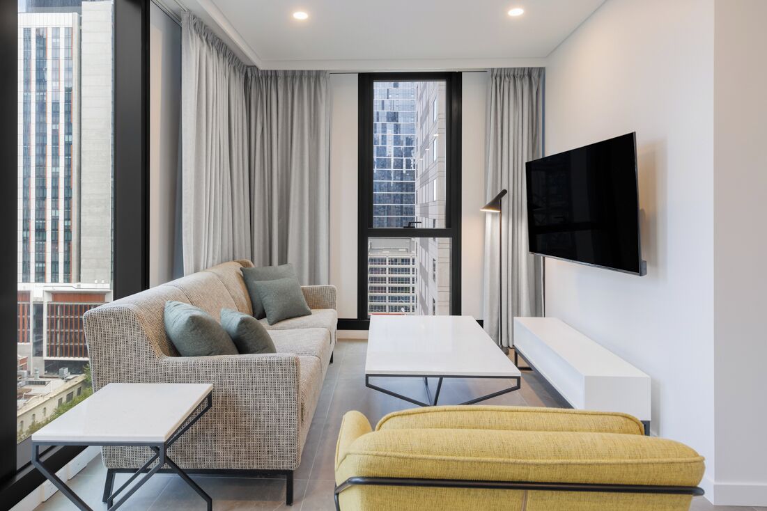 Un salon moderne avec un canapé, un fauteuil jaune, une table basse blanche et un téléviseur à écran plat fixé au mur.